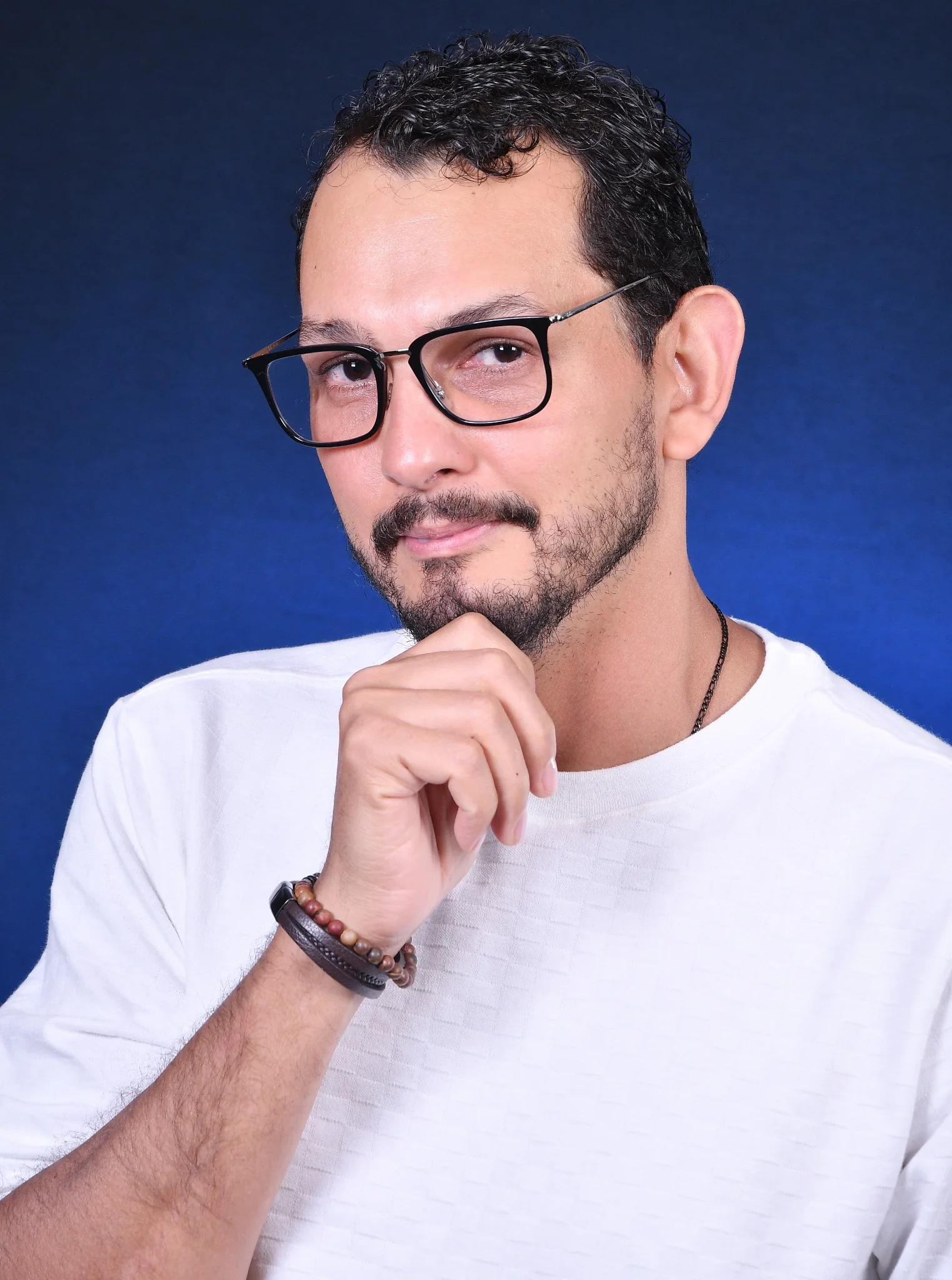 Daniel in a white jumper and glasses against a blue studio background